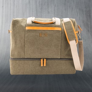 May include: Olive green canvas duffel bag with tan accents and a detachable shoulder strap. Features a front pocket with the initials "ES" in a brown color. Includes a separate bottom compartment and tan handles.