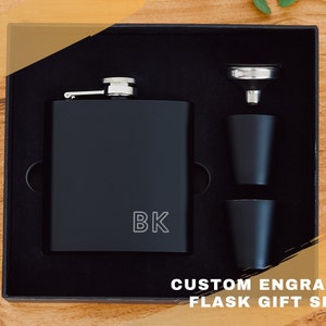 May include: A black flask gift set with a custom engraved inscription "BK" on the flask. The set includes a funnel and two shot glasses.