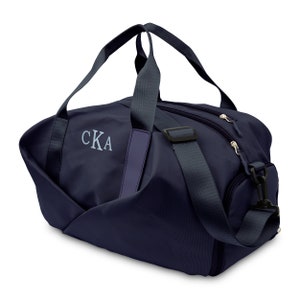 May include: A navy blue duffel bag with a zippered closure and a shoulder strap. The bag has a monogrammed "CKA" on the front.