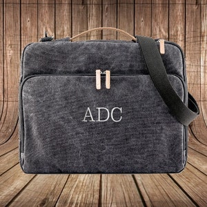 May include: A black canvas laptop bag with a leather handle and a shoulder strap. The bag has a zipper closure and the initials "ADC" are embroidered on the front.