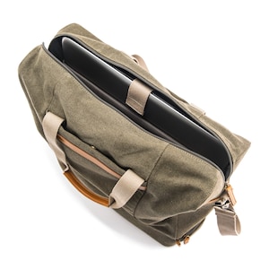 May include: An open, olive green canvas laptop bag with a black laptop inside. The bag has tan handles, straps, and trim. The zipper is open, and the bag is set against a white background.