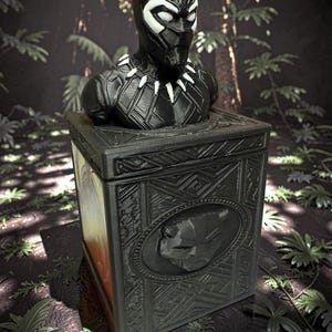 Op de afbeelding: Een zwart-witte buste van Black Panther op een bijpassende doos. De buste heeft gedetailleerde gelaatstrekken en een halsketting. De doos heeft een reliëfontwerp en een Black Panther-embleem, tegen een jungle-achtergrond.