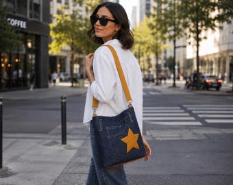 Könnte beinhalten: Eine dunkelblaue Umhängetasche aus Denim mit einem auffälligen, senfgelben Stern-Applikation auf der Vorderseite. Die Tasche verfügt über einen passenden, verstellbaren senfgelben Schulterriemen mit silberfarbenen Metallbeschlägen und Reißverschluss.