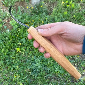 Peut inclure: Un couteau à sculpter en bois avec une lame incurvée. Le manche est en bois clair et présente un design à facettes. La lame est argentée et incurvée, adaptée aux travaux de menuiserie détaillés.