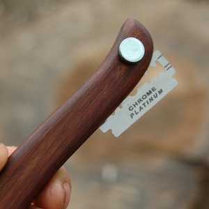 May include: A dark brown wooden straight razor handle with a silver metal rivet. A chrome platinum razor blade is inserted into the handle. The handle is curved and ergonomic.