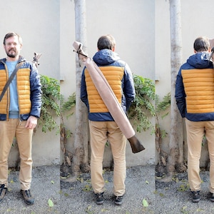 Peut inclure: Une personne portant une veste matelassée bleue et dorée et un pantalon beige, portant un long étui beige avec une extrémité marron foncé. L'étui est porté sur l'épaule avec une sangle marron. La veste a une capuche bleue et un pull bleu clair.