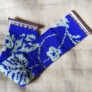 May include: A blue and white beaded bracelet with a floral pattern. The bracelet has silver metal clasps on each end.
