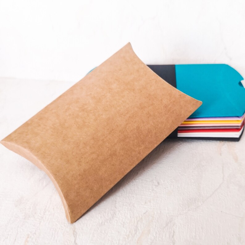 May include: A brown cardboard pillow box with a stack of colorful paper inside. The box is open and the paper is visible.