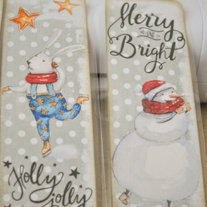 May include: Four Christmas-themed bookmarks with a gray background and white polka dots. The bookmarks feature a reindeer, a rabbit ice skating, a snowman, and the text "Merry and Bright".