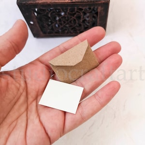 May include: A small brown envelope with a white card inside. The envelope and card are being held in a hand.