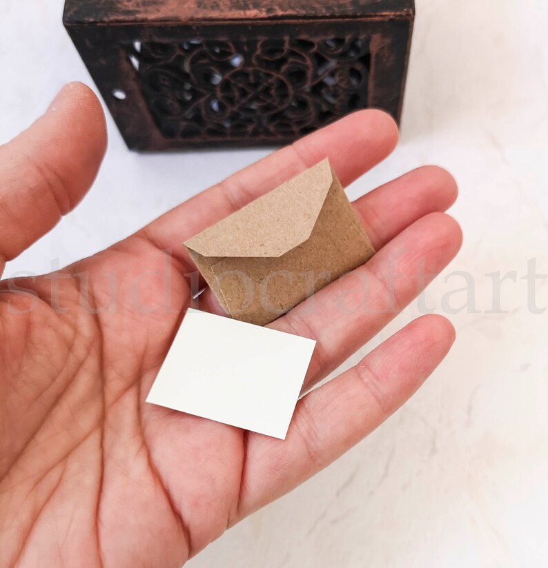 May include: A small brown envelope with a white card inside. The envelope and card are being held in a hand.