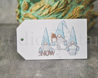 Pode incluir: Uma etiqueta branca com uma ilustração em aquarela de quatro gnomos e um boneco de neve. Os gnomos usam chapéus azuis e seguram um balde de bolas de neve. A palavra "SNOW" está escrita em letras marrons.