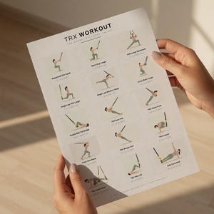 May include: A white printed workout guide titled "TRX WORKOUT FOR WOMEN FULL BODY - AS MIN". The guide displays illustrated exercises with instructions. The guide is held by a person with manicured nails.