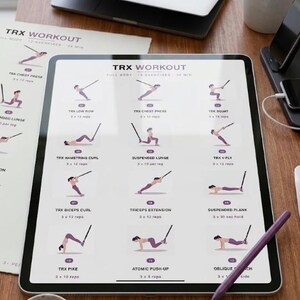 May include: A digital tablet displays a TRX workout routine with illustrations of exercises. The tablet is on a wooden surface, accompanied by printed workout sheets, a laptop, a pen, and a coffee mug. A small succulent plant is also visible.