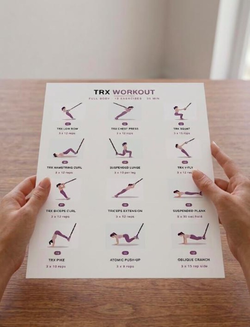May include: A white printed workout guide titled "TRX WORKOUT" with exercise illustrations. The guide includes exercises like TRX Low Row, Chest Press, and Squat. The guide is held by two hands.