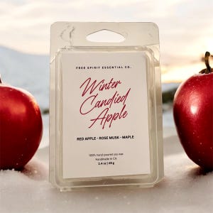 May include: A clear plastic package containing a soy wax melt. The label reads "Winter Candied Apple" with scent notes of red apple, rose musk, and maple. Two red apples flank the package. The wax melt weighs 2.4 oz (68 g).