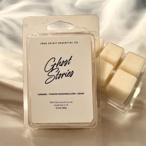 May include: A white wax melt in a clear plastic container with the text "Ghost Stories" in black cursive font. The wax melt is labeled "Caramel - Toasted Marshmallows - Cedar" and is 100% hand-poured soy wax, handmade in CA. The wax melt is 2.4 oz (68 g).