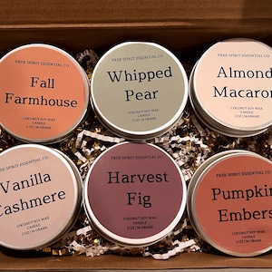 May include: A set of six round metal tins containing coconut soy wax candles, each labeled with Free Spirit Essential Co and a scent name: Fall Farmhouse, Whipped Pear, Almond Macaron, Vanilla Cashmere, Harvest Fig, and Pumpkin Embers, 2 oz.