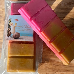 May include: A close-up of wax melts in a clear plastic package and a single wax melt bar. The wax melts are in shades of pink, yellow, and orange. The package has a label that says "Coconut Colada".