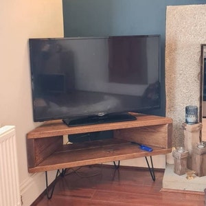 Peut inclure: Un meuble TV d'angle marron fonc&eacute; de forme rectangulaire avec des pieds &eacute;pingles. Le meuble dispose d'une &eacute;tag&egrave;re ouverte et supporte un grand t&eacute;l&eacute;viseur &agrave; &eacute;cran plat noir. Le meuble est en bois et a une finition naturelle.