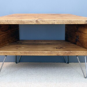 Peut inclure: Table basse rectangulaire en bois avec une finition naturelle. La table a un centre creux et est soutenue par quatre pieds en &eacute;pingle &agrave; cheveux argent&eacute;s. Le grain du bois est visible. Dimensions: environ 90 cm x 60 cm.