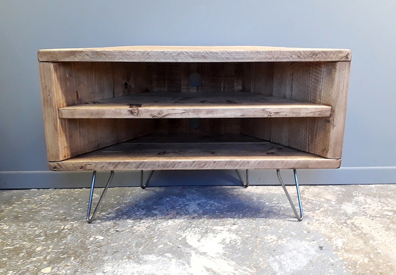 K&ouml;nnte beinhalten: Ein Eck-TV-St&auml;nder aus recyceltem Holz mit zwei Regalen und Haarnadelbeinen. Der St&auml;nder ist hellbraun und hat einen rustikalen Look.