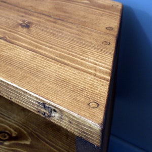 Peut inclure: Gros plan sur un coin de table en bois. La table est en bois brun clair avec des veines visibles et est construite avec des vis apparentes. Le coin est l&eacute;g&egrave;rement arrondi et le bois a une finition naturelle et chaleureuse.