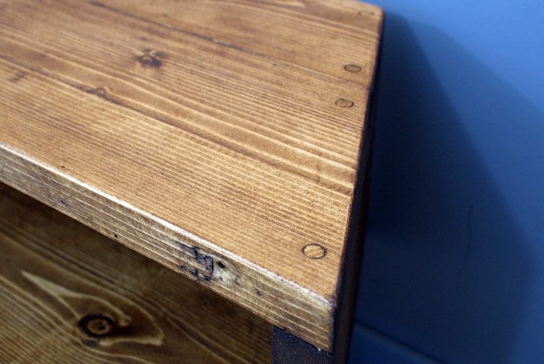 Peut inclure: Gros plan sur un coin de table en bois. La table est en bois brun clair avec des veines visibles et est construite avec des vis apparentes. Le coin est l&eacute;g&egrave;rement arrondi et le bois a une finition naturelle et chaleureuse.