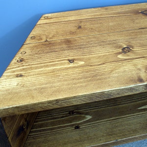 Peut inclure: Banc en bois de forme triangulaire avec une finition naturelle. Le banc est fabriqu&eacute; &agrave; partir de planches de bois, avec des n&oelig;uds et des motifs de grain visibles. Le bois a une teinte brun dor&eacute; chaud, et le banc semble robuste et bien fait.
