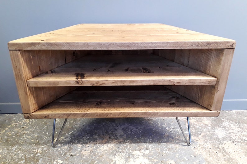 K&ouml;nnte beinhalten: Ein Eck-TV-St&auml;nder aus recyceltem Holz mit zwei Regalen und Haarnadelbeinen. Der St&auml;nder ist in einem hellen Braunton gebeizt.