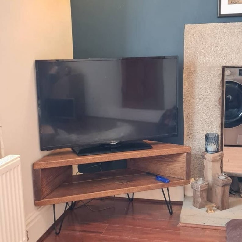 Peut inclure: Un meuble TV d'angle marron fonc&eacute; de forme rectangulaire avec des pieds &eacute;pingles. Le meuble dispose d'une &eacute;tag&egrave;re ouverte et supporte un grand t&eacute;l&eacute;viseur &agrave; &eacute;cran plat noir. Le meuble est en bois et a une finition naturelle.