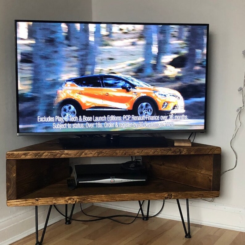 Peut inclure: Un meuble TV d'angle marron fonc&eacute;, de forme rectangulaire, avec des pieds &eacute;pingles. Un t&eacute;l&eacute;viseur &agrave; &eacute;cran plat affiche une publicit&eacute; de voiture. Le meuble a une &eacute;tag&egrave;re avec un lecteur multim&eacute;dia noir. Le texte est affich&eacute; sur l'&eacute;cran du t&eacute;l&eacute;viseur.