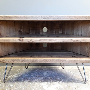 K&ouml;nnte beinhalten: Ein Eck-TV-St&auml;nder aus recyceltem Holz mit zwei Regalen und Haarnadelbeinen. Der St&auml;nder hat zwei L&ouml;cher auf der R&uuml;ckseite f&uuml;r Kabel.