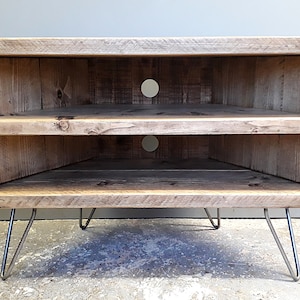 K&ouml;nnte beinhalten: Ein Eck-TV-St&auml;nder aus recyceltem Holz mit zwei Regalen und einer nat&uuml;rlichen Holzoptik. Der St&auml;nder hat Haarnadelbeine aus Metall.