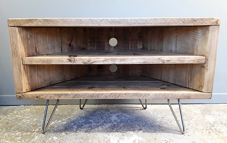 K&ouml;nnte beinhalten: Ein Eck-TV-St&auml;nder aus recyceltem Holz mit zwei Regalen und einer nat&uuml;rlichen Holzoptik. Der St&auml;nder hat Haarnadelbeine aus Metall.