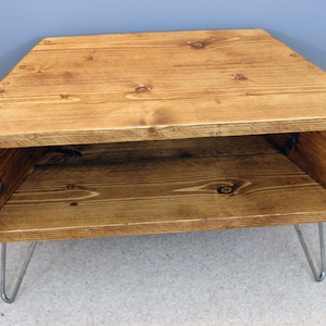 Peut inclure: Table d'appoint triangulaire en bois, avec une teinture brun chaud. Elle poss&egrave;de une &eacute;tag&egrave;re inf&eacute;rieure et repose sur des pieds &eacute;pingles argent&eacute;s. Le grain du bois est visible. La table mesure environ 76 cm de large.