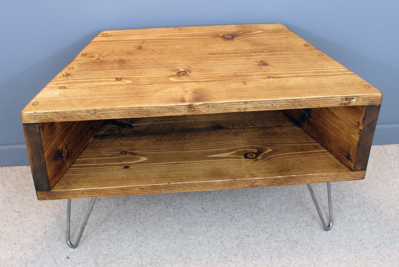 Peut inclure: Table d'appoint triangulaire en bois, avec une teinture brun chaud. Elle poss&egrave;de une &eacute;tag&egrave;re inf&eacute;rieure et repose sur des pieds &eacute;pingles argent&eacute;s. Le grain du bois est visible. La table mesure environ 76 cm de large.