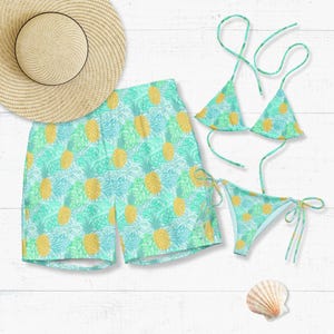 May include: A light blue and green pineapple-patterned swim set, including a bikini, swim trunks, and a straw sun hat. The bikini top and bottom have tie closures. A seashell is also present.