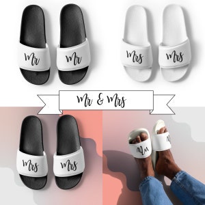Puede incluir: Dos pares de chanclas negras y blancas con las palabras "Mr" y "Mrs" impresas en ellas. Las chanclas están dispuestas en forma de cuadrado con una pancarta que dice "Mr & Mrs" encima.