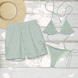 May include: A light green bikini set and matching shorts with a white polka dot pattern. A straw sun hat is also present. The swimwear features triangle tops and tie sides. The shorts have an elastic waistband.