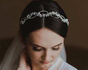 May include: A bride wearing a white robe with lace trim and a delicate pearl and crystal headband.