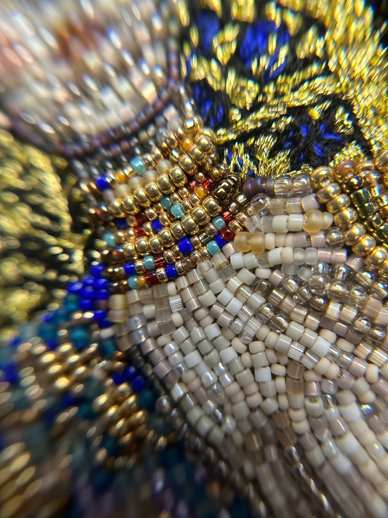 May include: Close-up of a beaded fabric with a variety of colors, including gold, white, blue, and red. The beads are arranged in a pattern that creates a textured surface.