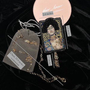 May include: A beaded necklace with a black and gold pendant featuring a portrait of a woman. The pendant is 1.7 inches tall and 3.5 inches wide. The chain is 29.9 inches long with an extension. The necklace comes in a pink box with the text "Your Amour" and "na Mankevych".