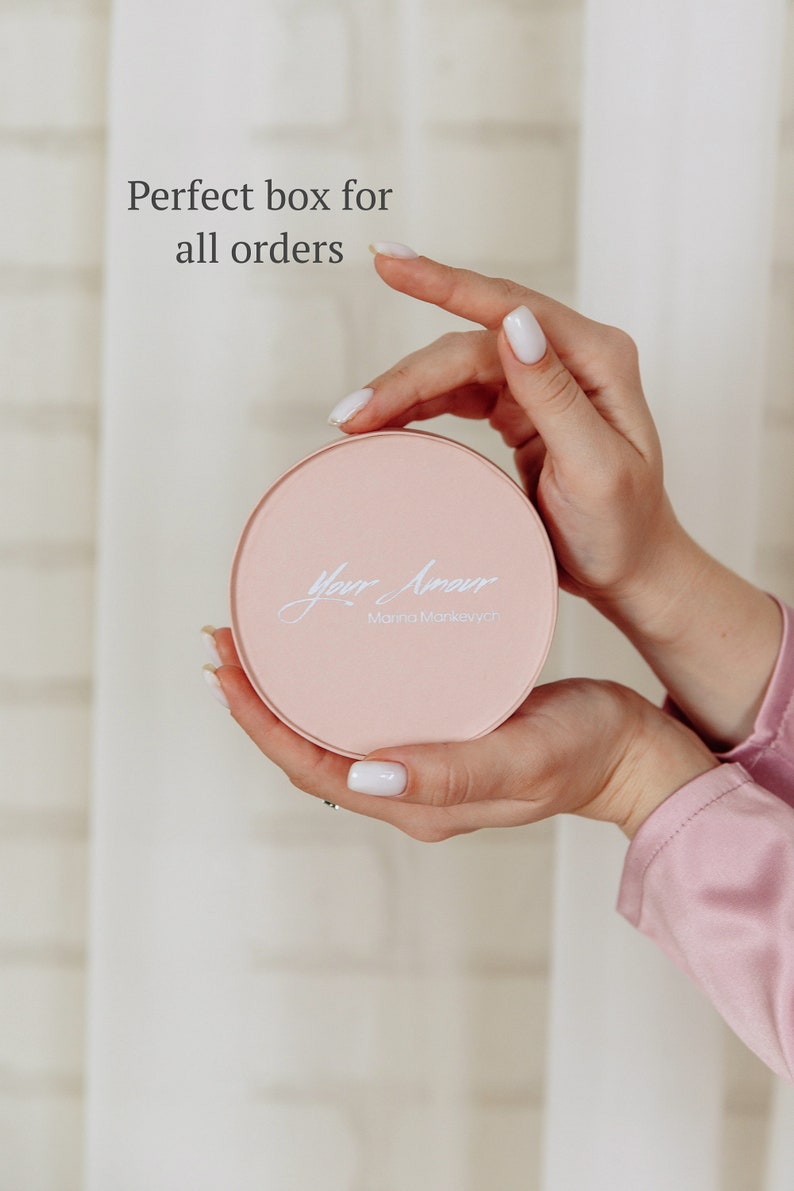 May include: A round, light pink box with the words "Your Amour" and "Marina Mankevych" in elegant script. The box is held in two hands with white nail polish. The text "Perfect box for all orders" is in the background.
