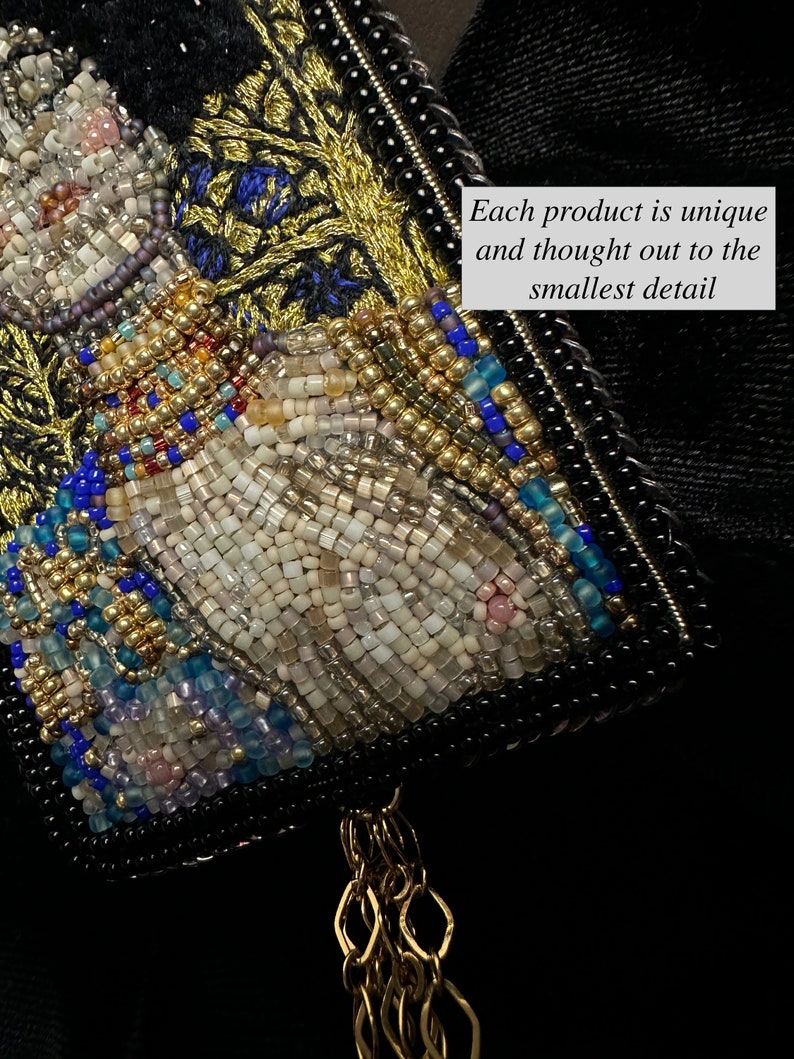 May include: A close-up of a beaded artwork featuring a white figure with gold and blue accents. The artwork is framed with black beads and has a gold chain tassel.