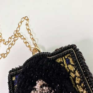 May include: A black beaded necklace with a gold chain and a black and gold embroidered pendant featuring a portrait of a person.