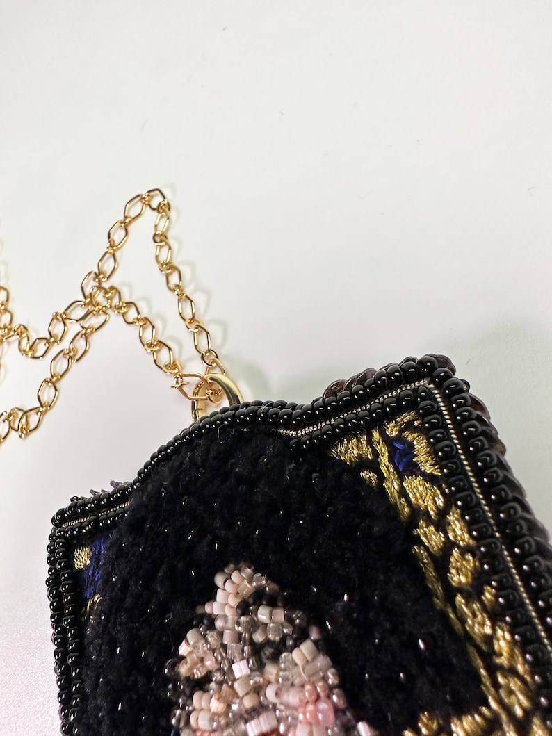 May include: A black beaded necklace with a gold chain and a black and gold embroidered pendant featuring a portrait of a person.