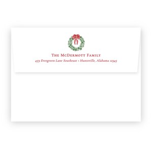 May include: White envelope with a watercolor Christmas wreath and red bow. The text "The McDermott Family" and address are printed in red. The envelope is for holiday cards.