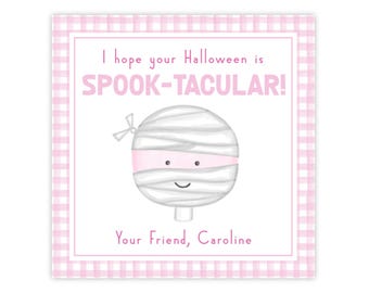 May include: A square gift tag with a light pink gingham border. The text reads I hope your Halloween is SPOOK-TACULAR! and Your Friend, Caroline. In the center is a round, white mummy character with a pink band across its eyes and a small bow.
