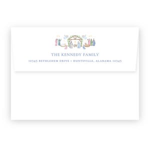 May include: A white envelope with a watercolor illustration of a nativity scene at the top. The text "THE KENNEDY FAMILY" is centered below the illustration, with the address below. The illustration features figures, angels, and a stable.